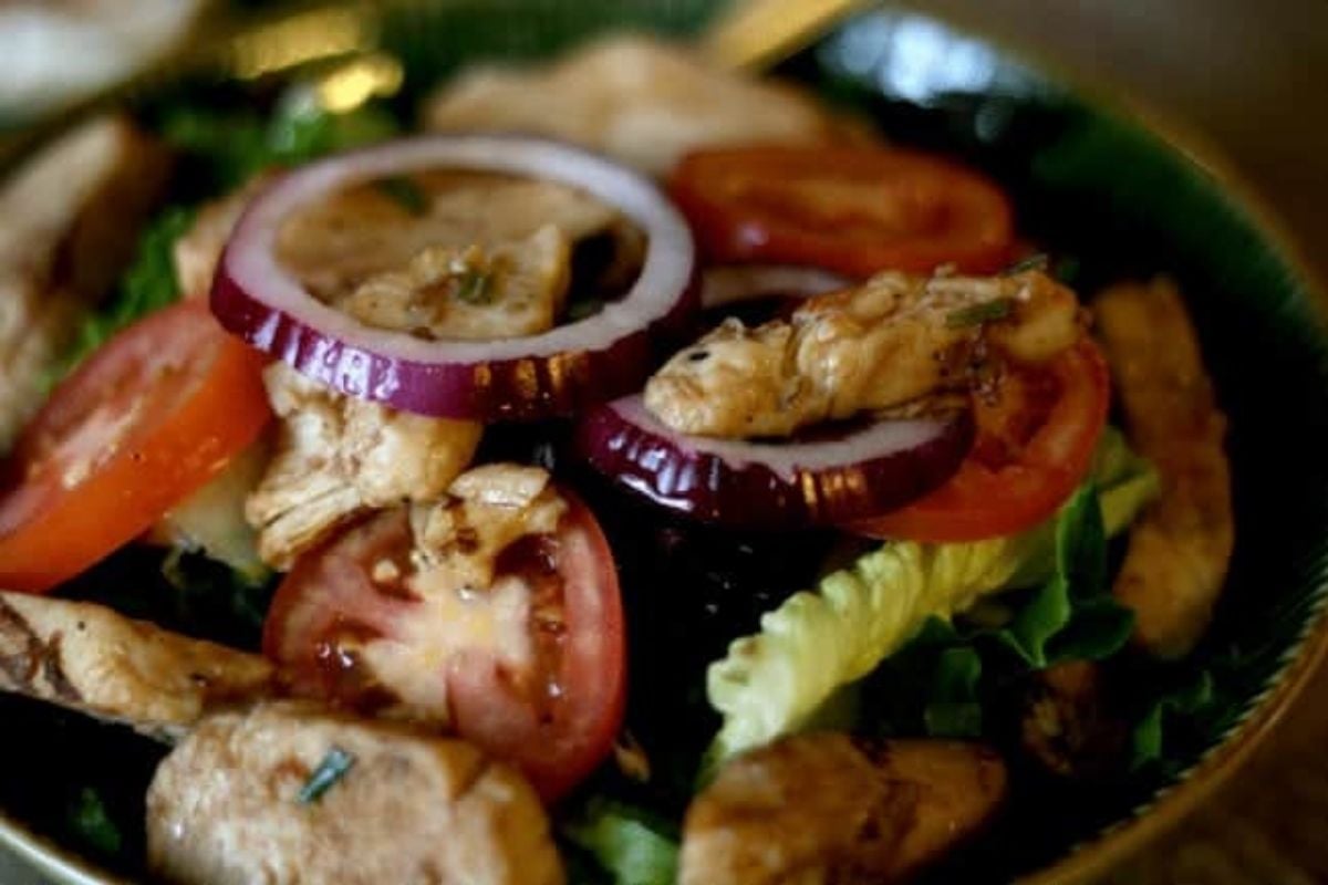Close up of balsamic chicken salad with tomato, red onion, and greens