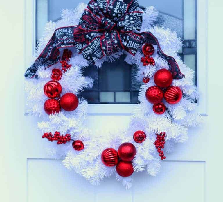 white Christmas wreath with clusters of red ornaments attached and a black, red, and white Christmas ribbon