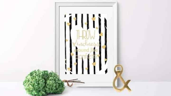 Throw Kindness Around Like Confetti - free printable shown in a white frame with a gold ampersand and bundle of dried green hydrangea on a white table with a white wall background