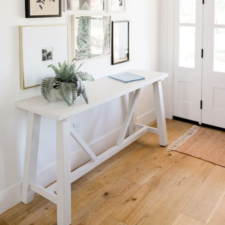 Entry way decor featuring a white sawhorse table with simple uncluttered decor that is welcoming