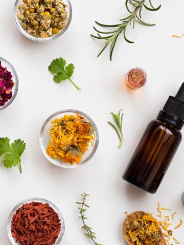 Overhead view of an ember glass fragrance dropper bottle surrounded by culinary herbs and spices