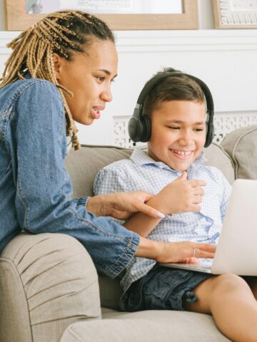 Young woman teaching a neurodivergent child with the aid of a laptop and headphones