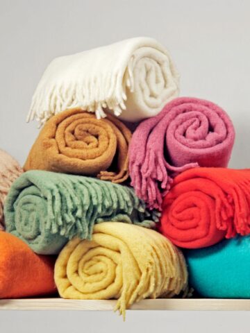 A neatly stacked collection of cozy, rolled fleece blankets in various colors, ideal for adding warmth and color to your home decor.