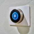 A modern smart thermostat mounted on a white wall, displaying a blue interface with the heat set to 63 degrees Fahrenheit. The sleek, circular design adds a touch of style to the device, making it both functional and visually appealing.