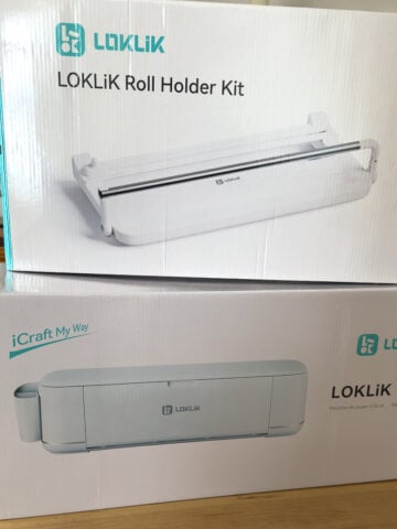 Two boxes stacked on a wooden table. The top box is labeled "LOKLiK Roll Holder Kit," and the bottom box is labeled "LOKLiK iCraft™" with an image of the cutting machine.