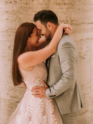 A radiant couple in a close embrace, with the bride in a soft pink lace gown and the groom in a fitted gray suit. Their genuine laughter and modern wedding style make for a perfect courthouse wedding inspiration.