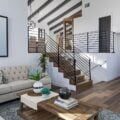 A chic yet budget-friendly living area with a tufted beige sofa, a wooden coffee table, and modern metal railings, blending rustic charm with contemporary style.