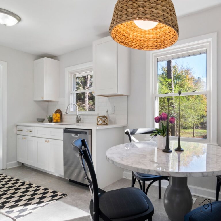 Bright, white kitchen with round marble table, woven pendant light, and clean, simple storage.