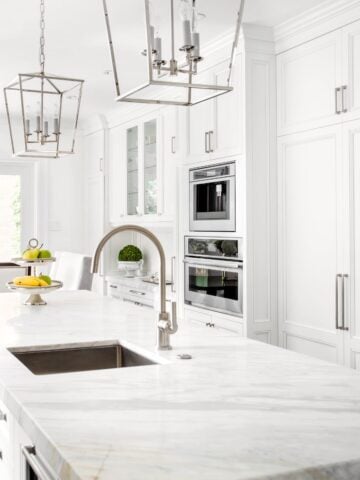 A stunning, all-white kitchen with a large marble island, stainless steel appliances, and elegant pendant lighting, showcasing a pristine and clutter-free space.