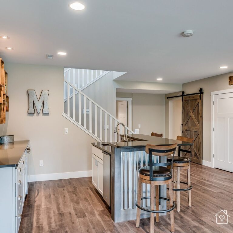 A beautifully renovated basement featuring a modern kitchenette with a rustic-style island, wooden barstools, and a sliding barn door. This home renovation showcases how mortgage financing can help homeowners create a stylish and functional living space.