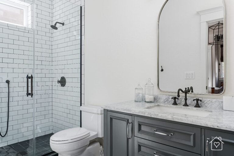 Modern black and white bathroom with subway tile shower and marble vanity, highlighting efficient and stylish plumbing fixtures.