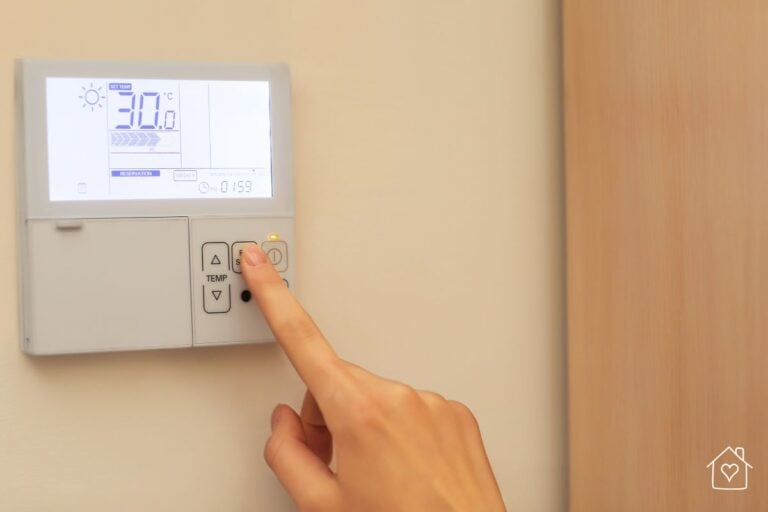 A hand pressing buttons on a digital thermostat set to cool the home to a comfortable temperature.
