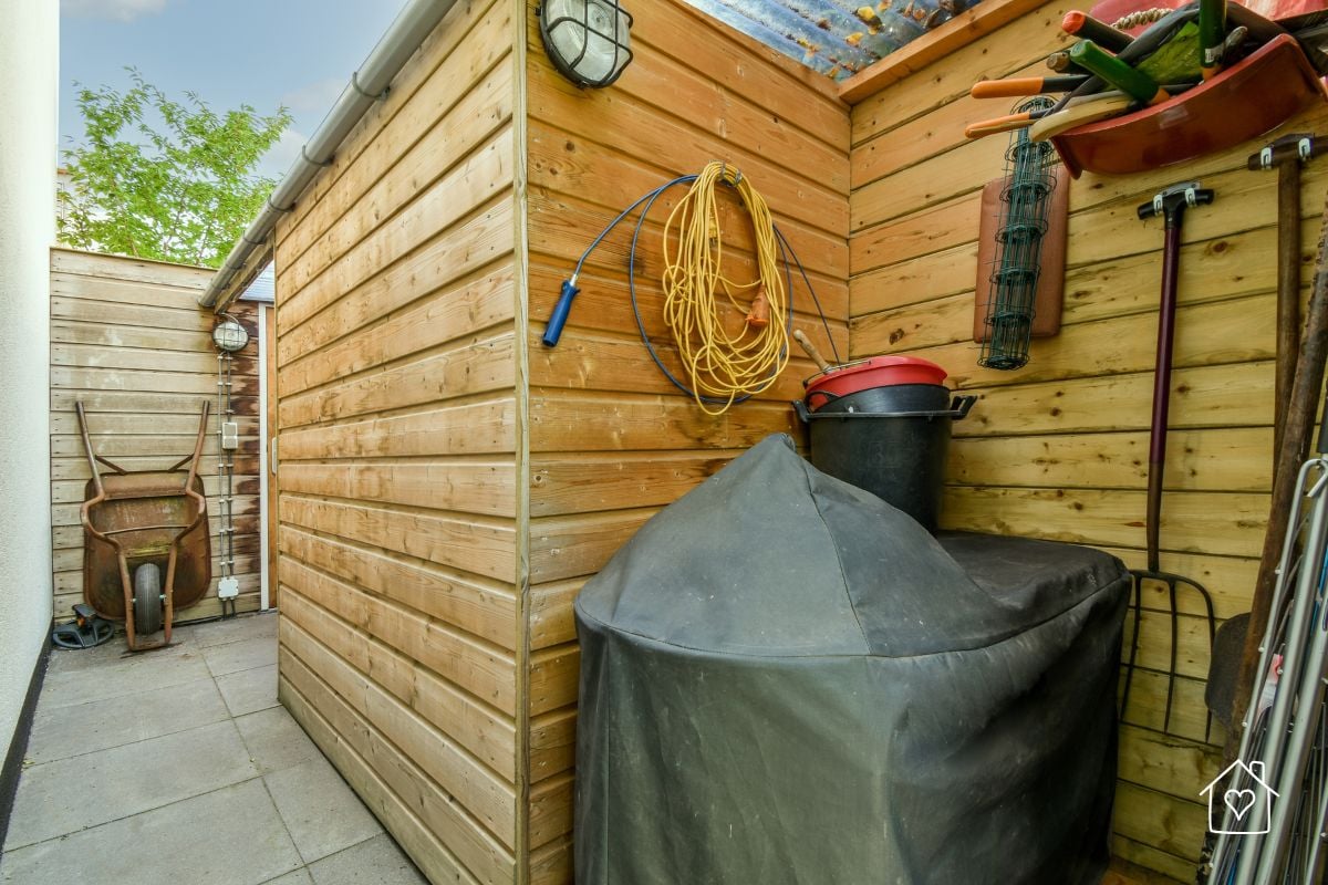 An outdoor shed wall used for organizing garden tools, cords, and equipment in a tidy space.