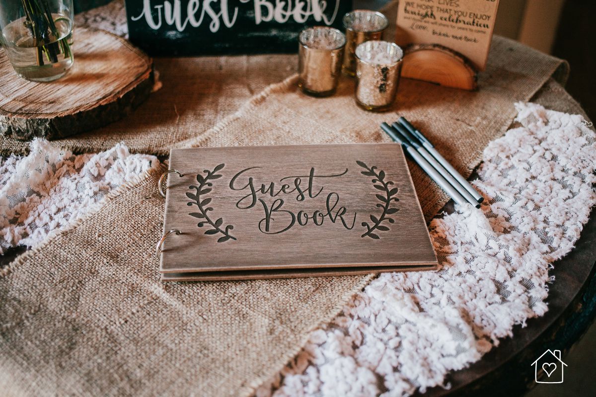 Rustic wooden guest book on a burlap and lace table with pens and décor, ideal for cozy weddings with personal touches.