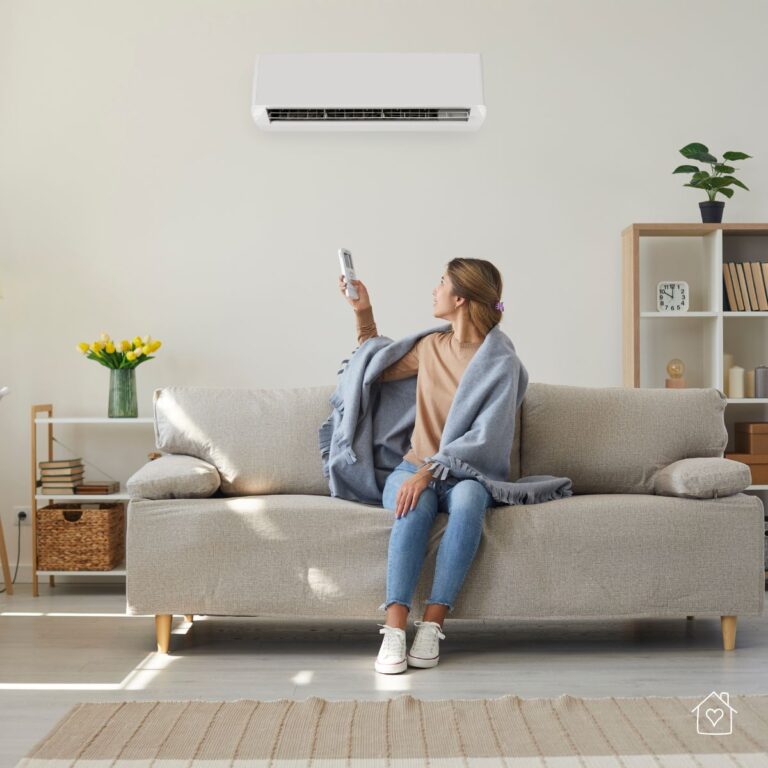 A woman wrapped in a blanket enjoying cool air from a wall-mounted AC unit, representing effective home cooling.