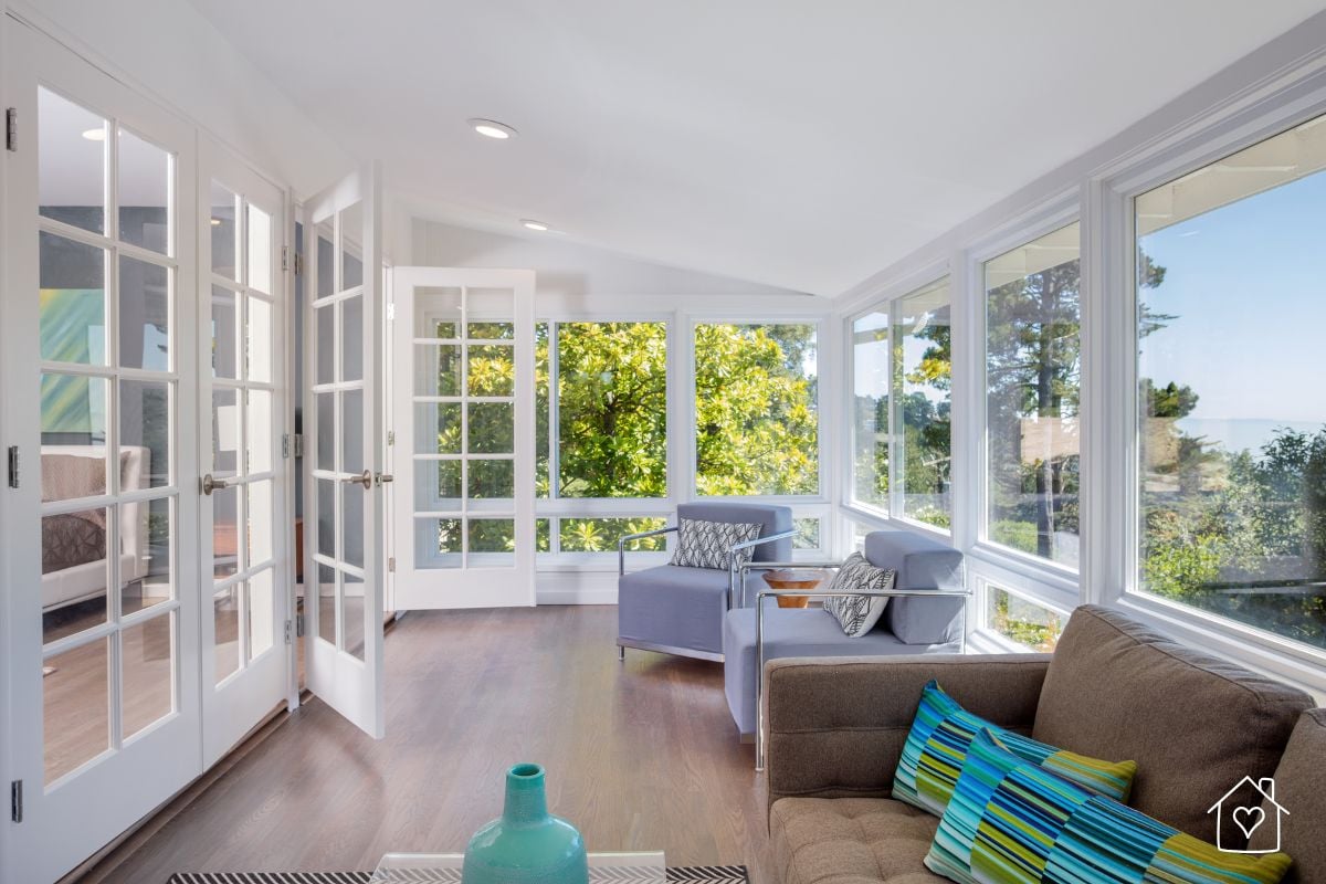 A cozy, light-filled sitting room with modern armchairs and French doors, showcasing a flexible living area that adapts to seasonal use.