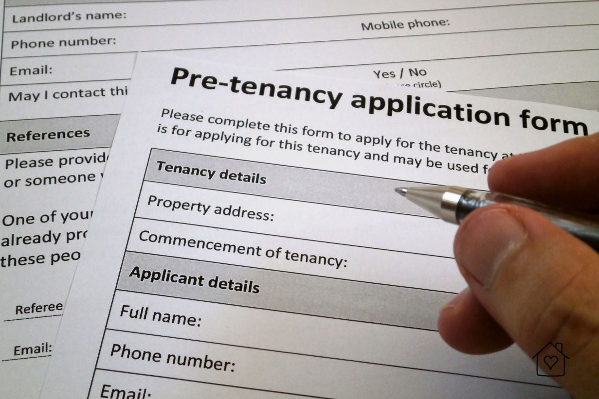 Hand holding a pen over a pre-tenancy application form used for tenant background checks and screening process.