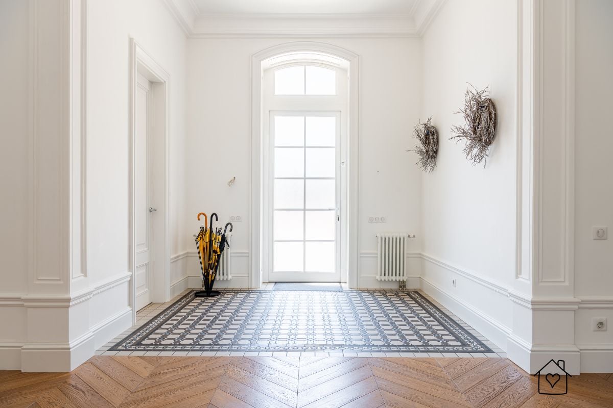 Sophisticated entryway with a decorative tile inlay bordered by herringbone wood flooring, highlighting classic architectural details.