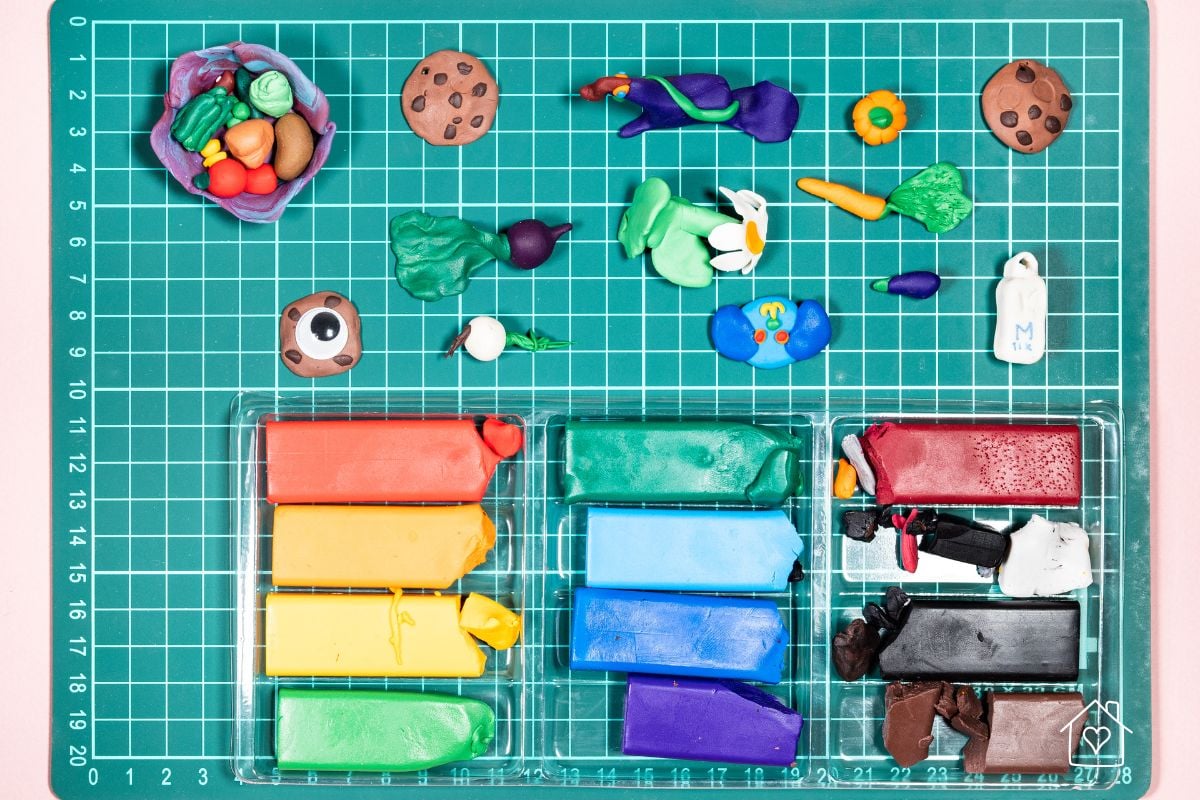 A cutting mat with various polymer clay creations and a colorful set of clay bars, perfect for beginners crafting miniatures like cookies, vegetables, and flowers.