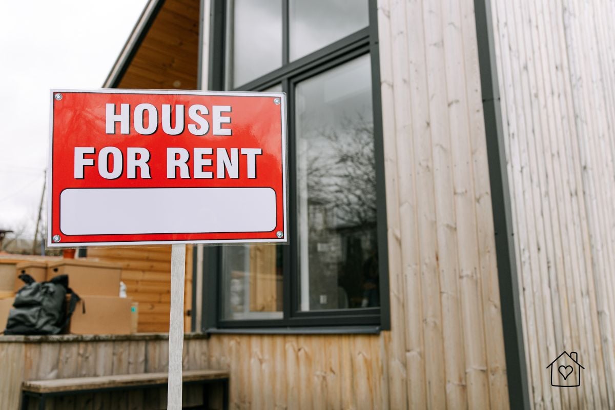 Bright red "House for Rent" sign placed in front of a wooden house, highlighting the importance of background checks before approving tenants.
