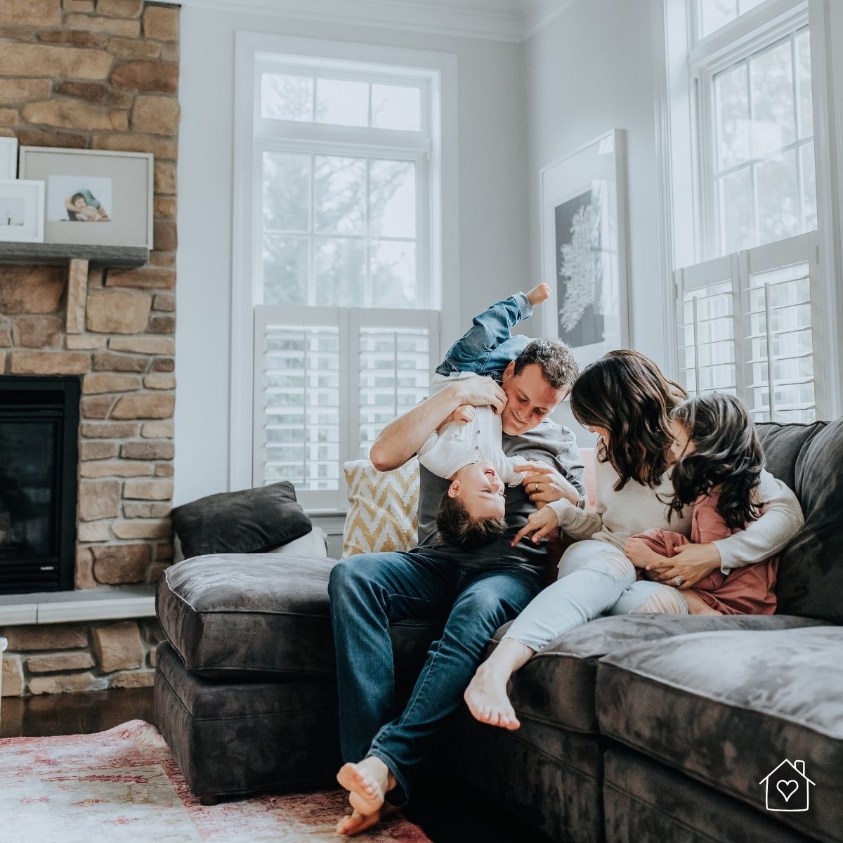 A joyful family laughing and cuddling together on a tidy sectional sofa in a bright living room—showcasing the peace and connection that followed the deep cleaning process.