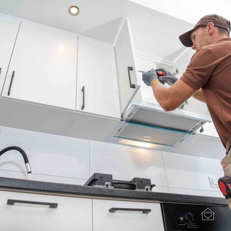 A handyman using a screwdriver to secure white cabinet doors above a stovetop as part of a kitchen cabinet refacing process.
