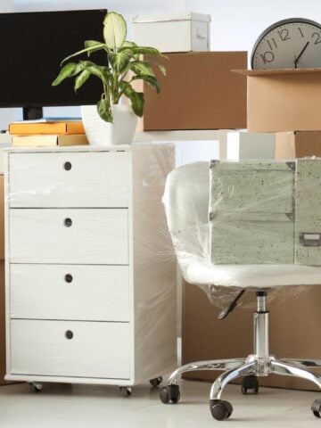 Home office in transition with cardboard boxes and plastic storage containers for organizing work essentials.