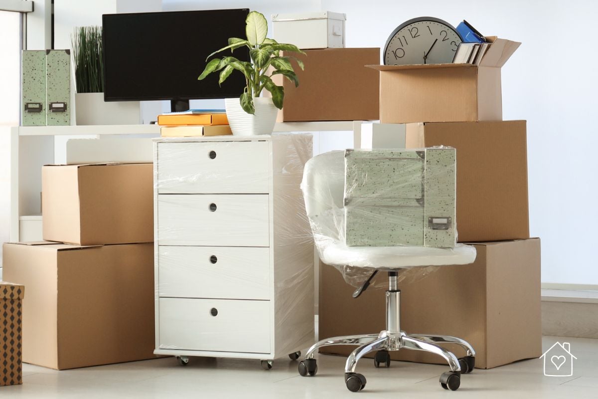Home office in transition with cardboard boxes and plastic storage containers for organizing work essentials.
