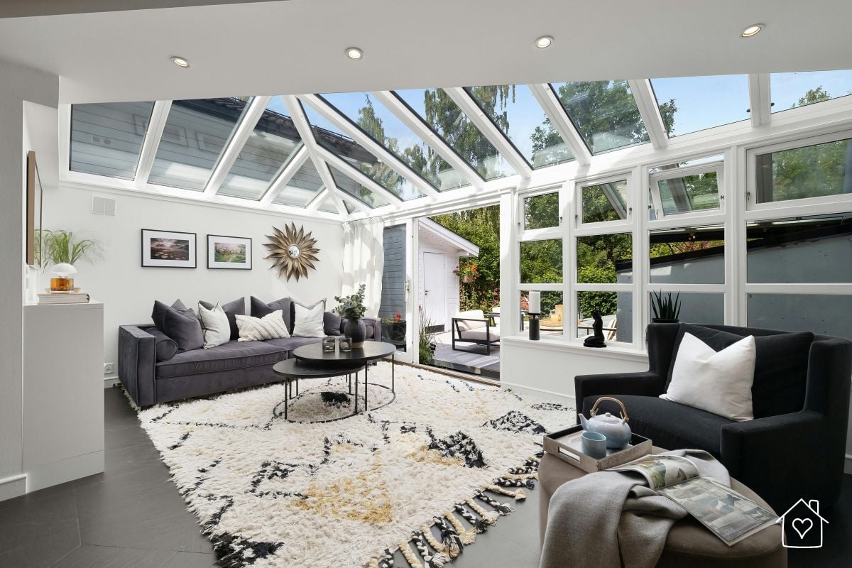 A contemporary sunroom with a glass ceiling and sleek furniture, used as a year-round flexible living area blending indoor and outdoor comfort.