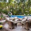 Outdoor living area featuring a stamped tile patio around a stone fire pit and pool, surrounded by lush landscaping and wicker seating.
