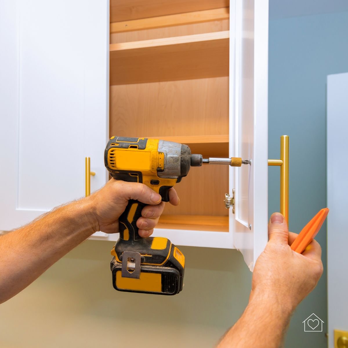 Close-up of a yellow power drill being used to install new gold hardware onto a freshly refaced white kitchen cabinet.