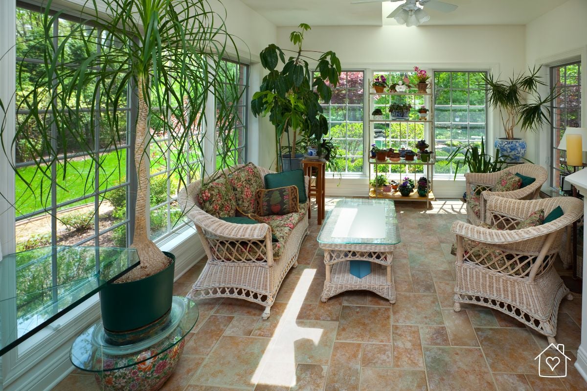 A garden room filled with natural light, wicker furniture, and thriving plants, serving as a flexible living area ideal for relaxation or entertaining.