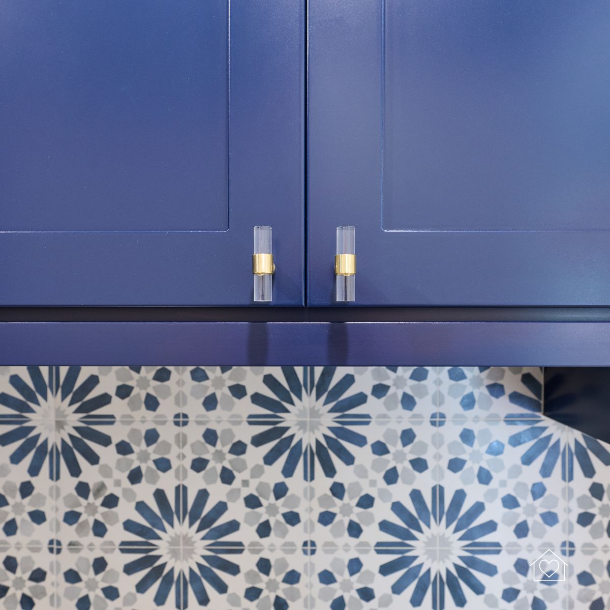 Blue kitchen cabinets with modern acrylic and brass hardware set against a patterned backsplash, highlighting a completed cabinet refacing project.