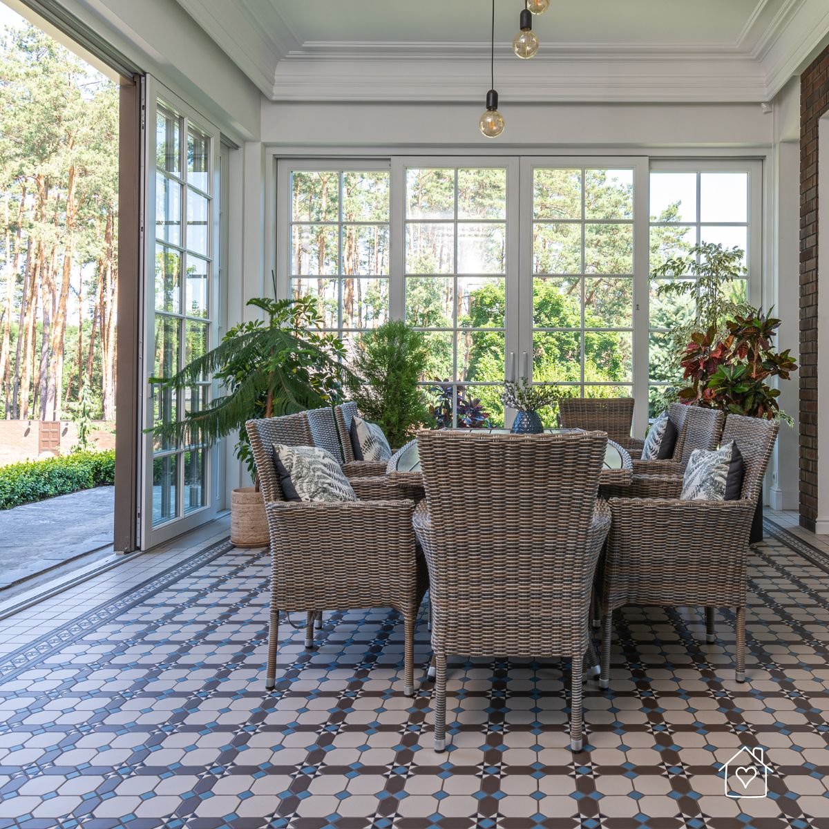 A bright enclosed patio with wicker dining furniture and tiled flooring, designed as a flexible living area for indoor-outdoor gatherings.