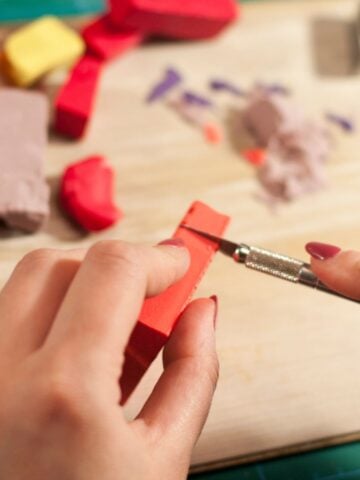 Close-up of hands cutting red polymer clay with a craft knife, showing how beginners can shape and sculpt their clay for detailed projects.