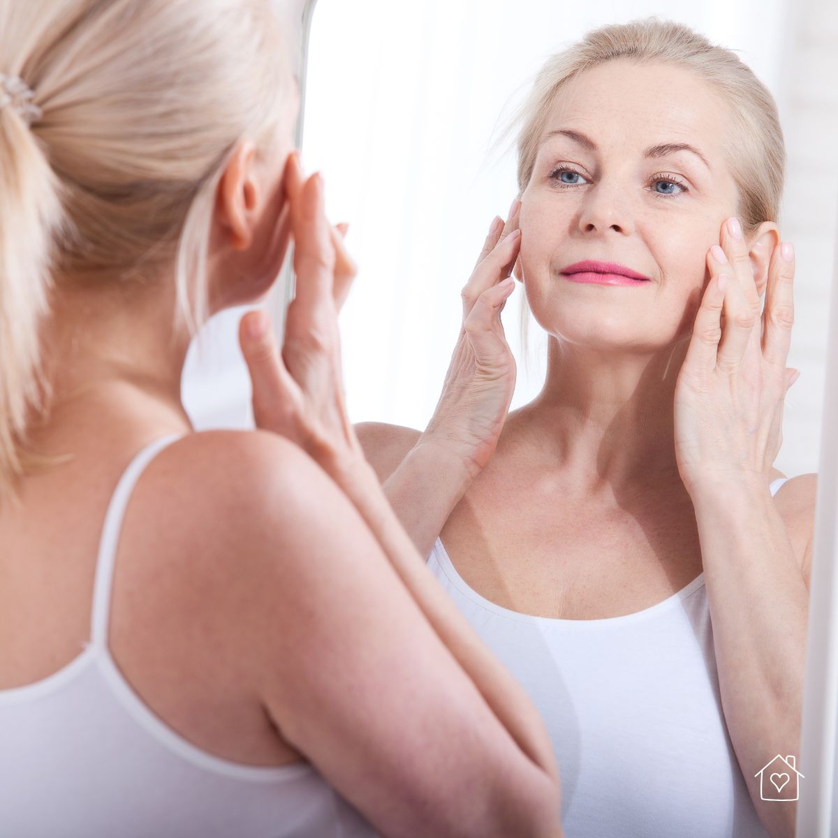Mature woman examining her face in the mirror, checking for signs of skin aging and elasticity.