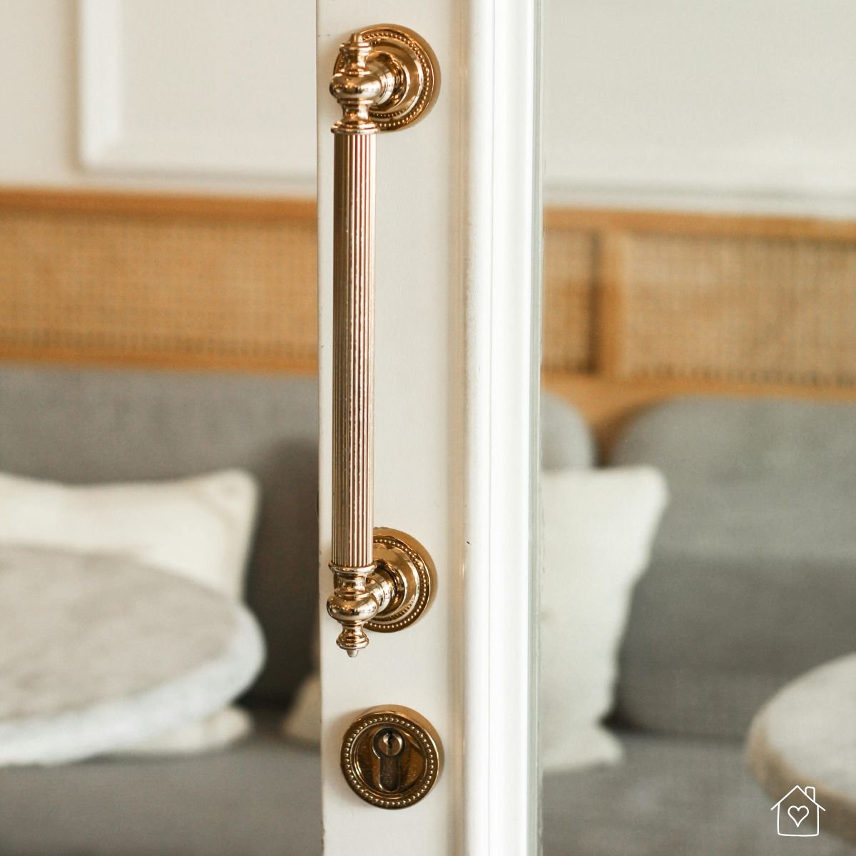 Close-up of a gold vintage-style door handle on a white door with cozy neutral living room in the background
