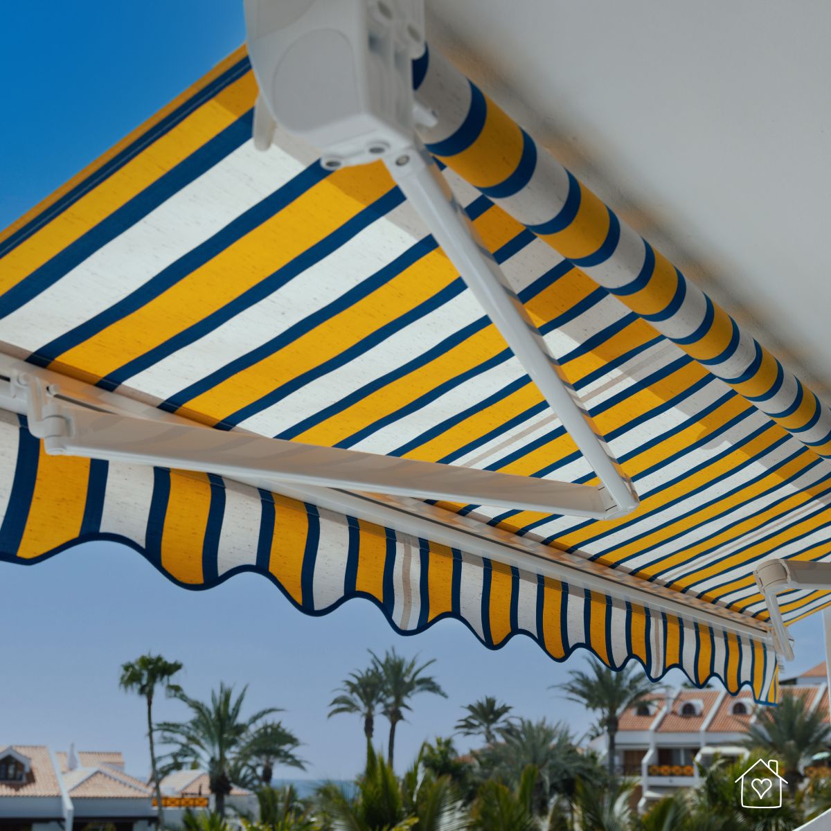 Yellow, white, and blue striped retractable awning installed over a balcony with palm trees and rooftops in the background.