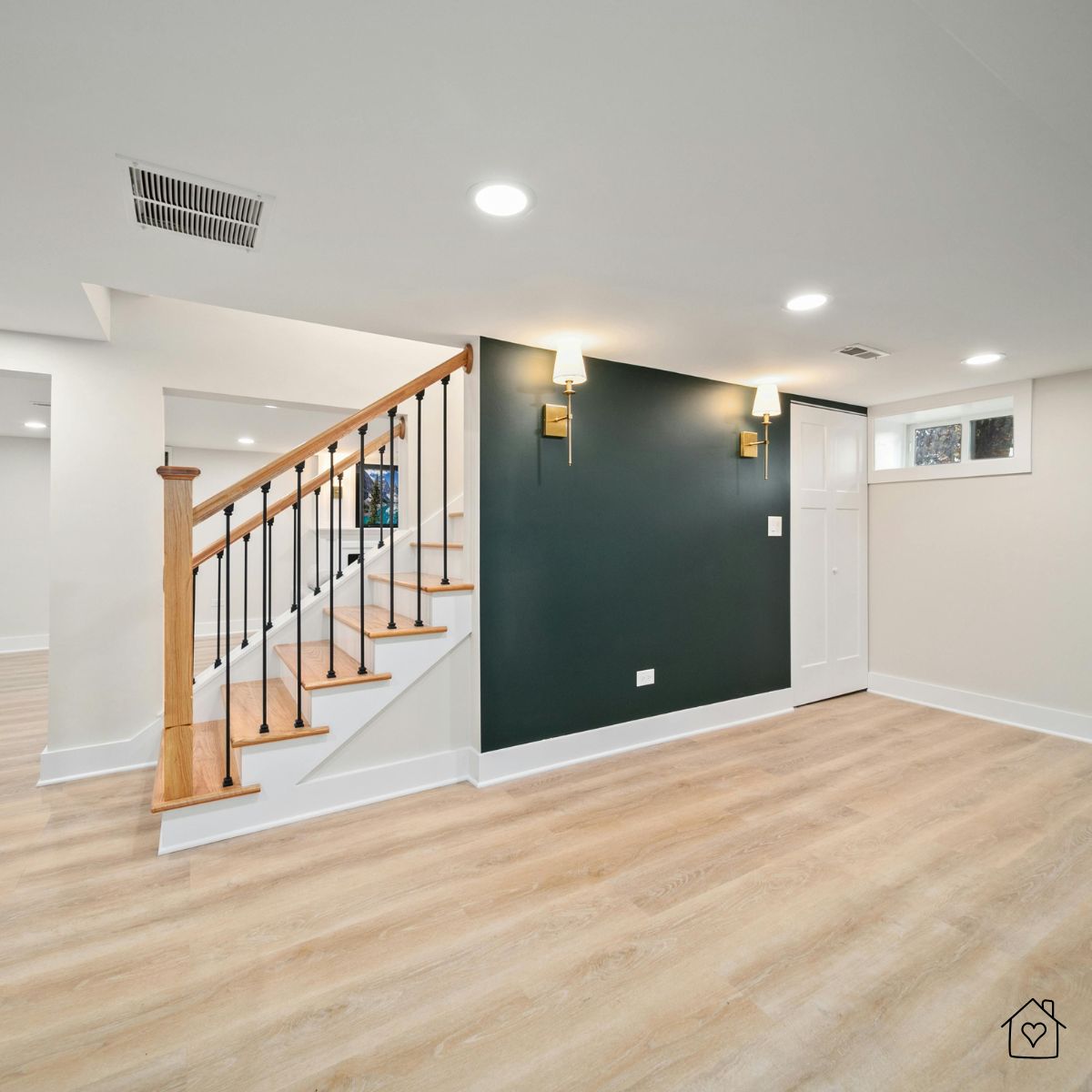 Renovated basement featuring light wood flooring, black-accented staircase, and modern lighting—showing what a properly insulated basement can look like