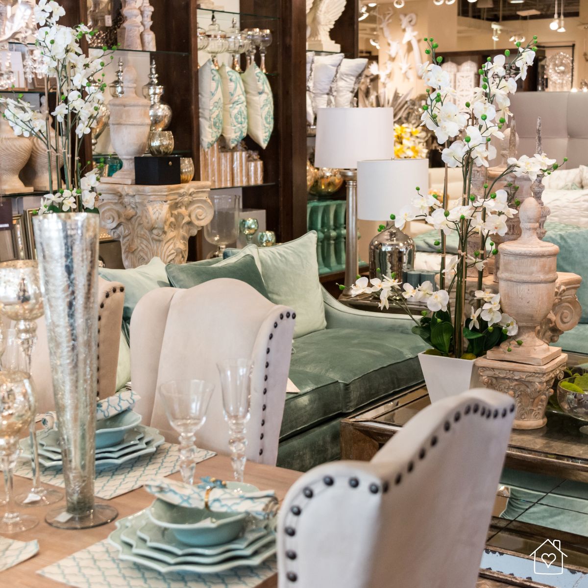 Upscale home store display featuring plush seating, decorative pillows, ornate vases, and a formal dining table setting.
