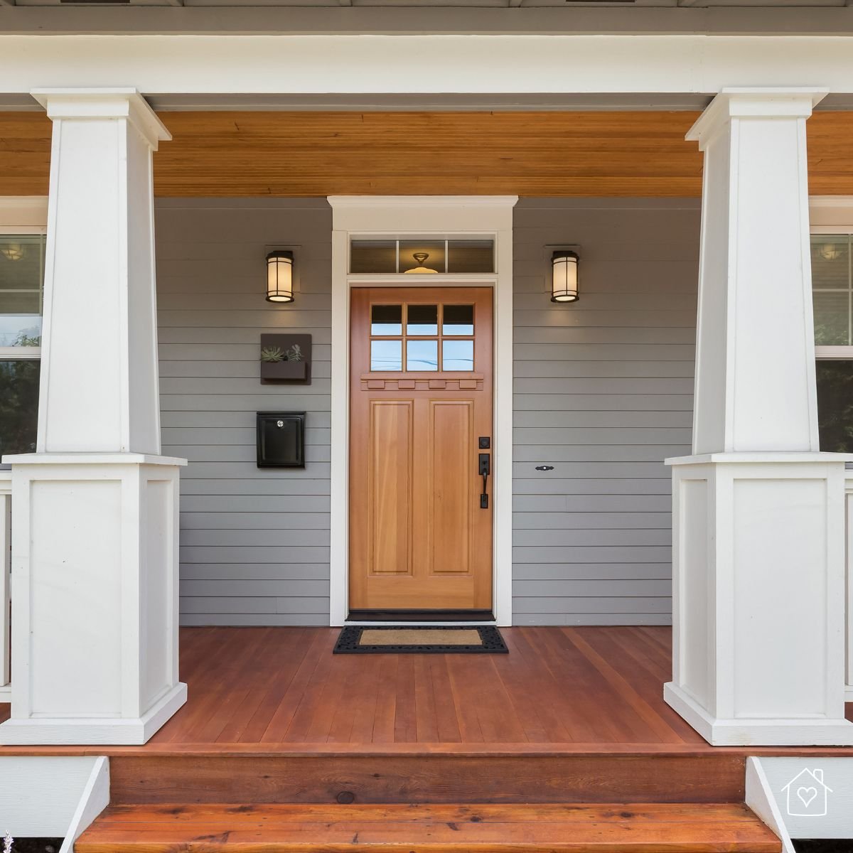 Sturdy wooden front door on a gray house with a covered porch and white columns, protected from rain and sun.