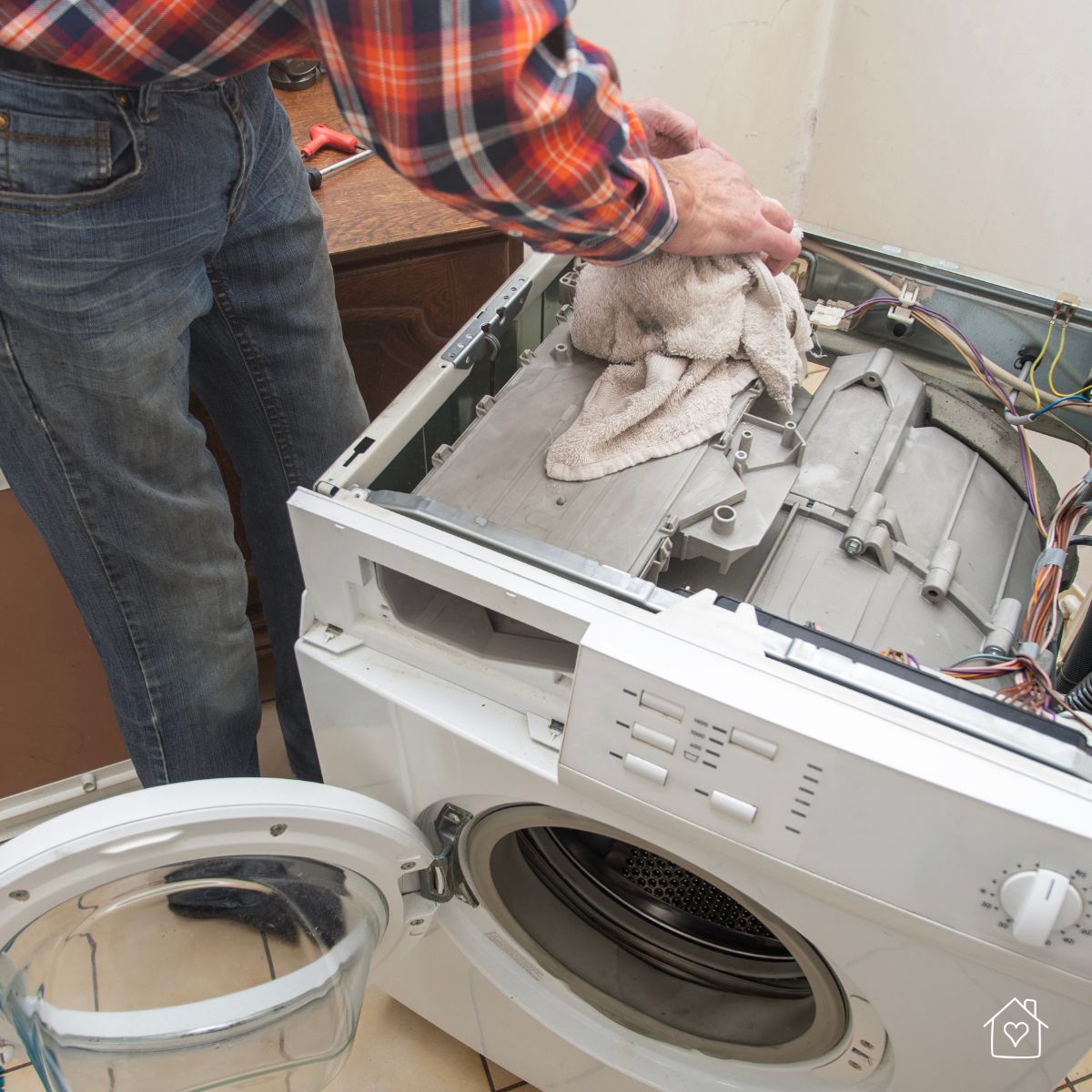 Technician using a towel while repairing a washing machine, showing hands-on maintenance work with the top panel removed.