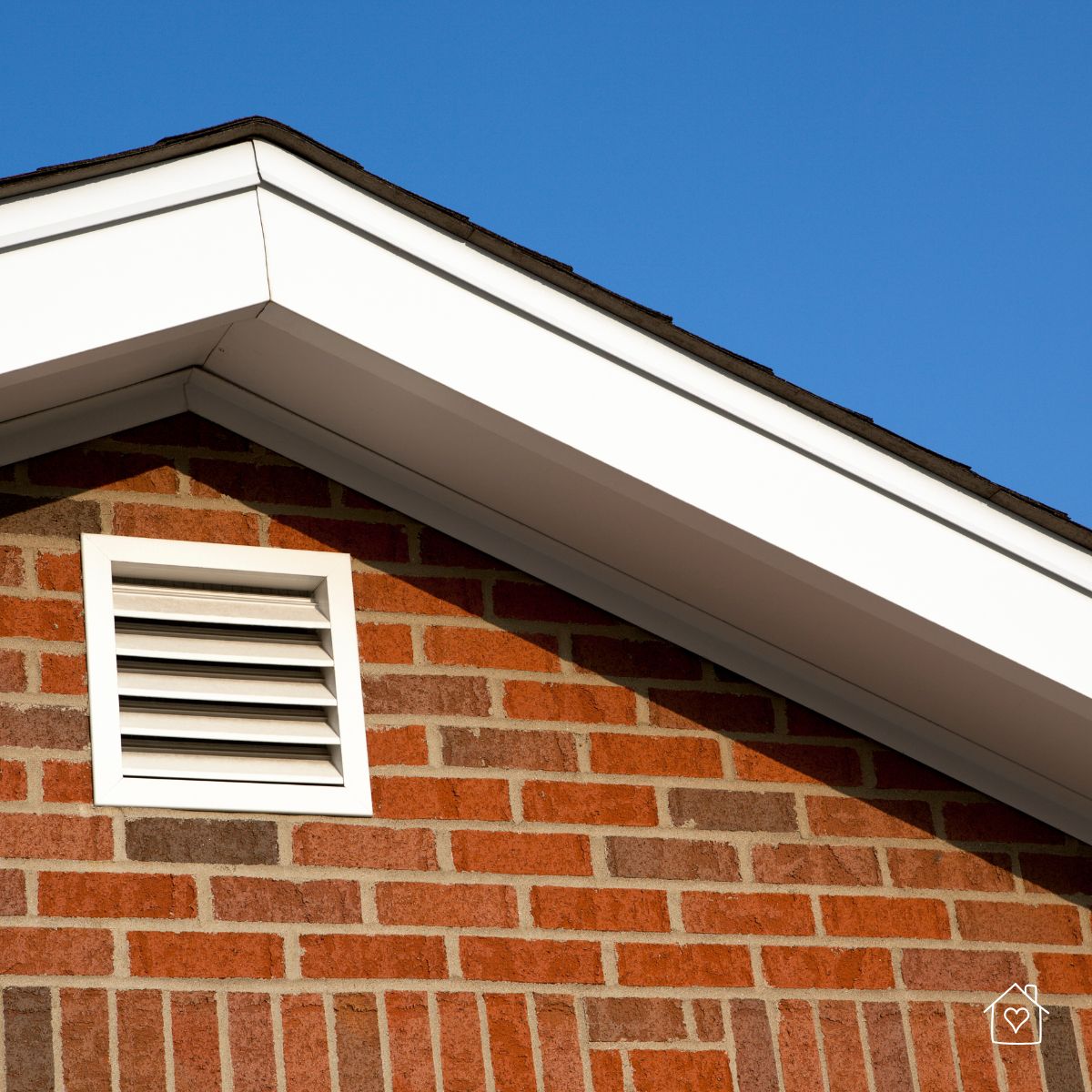 Brick home with a white attic vent under the roofline, essential for ventilation and moisture prevention.