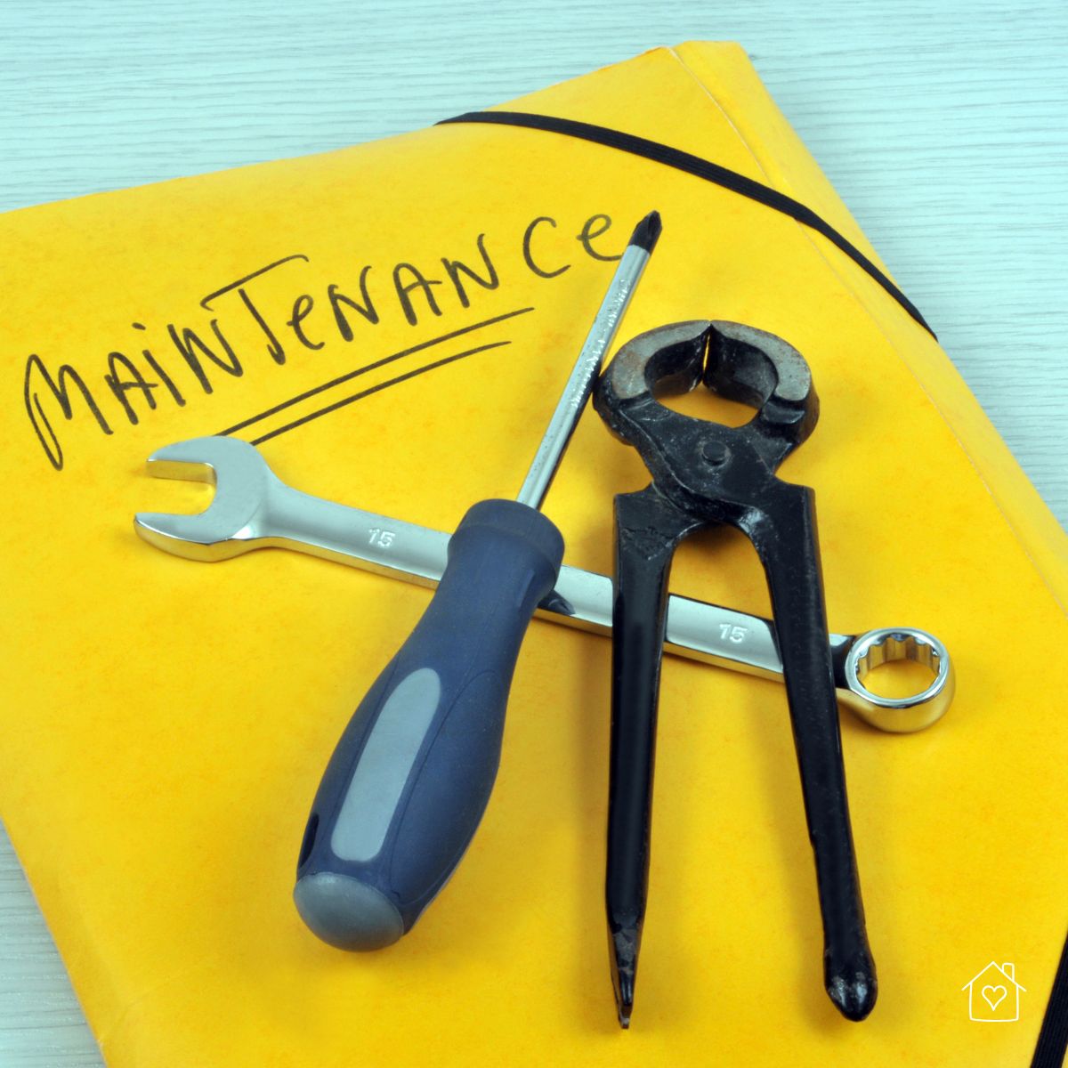 Maintenance folder with a screwdriver, wrench, and pliers on top, representing tools for home exterior upkeep.