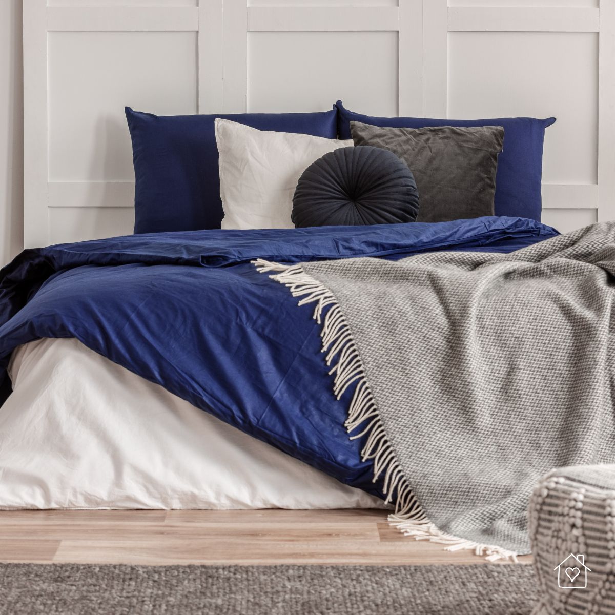 A stylish bed featuring rich navy blue bedding, a mix of pillows, and a soft gray throw, set against a paneled white wall for a calm, tailored look.