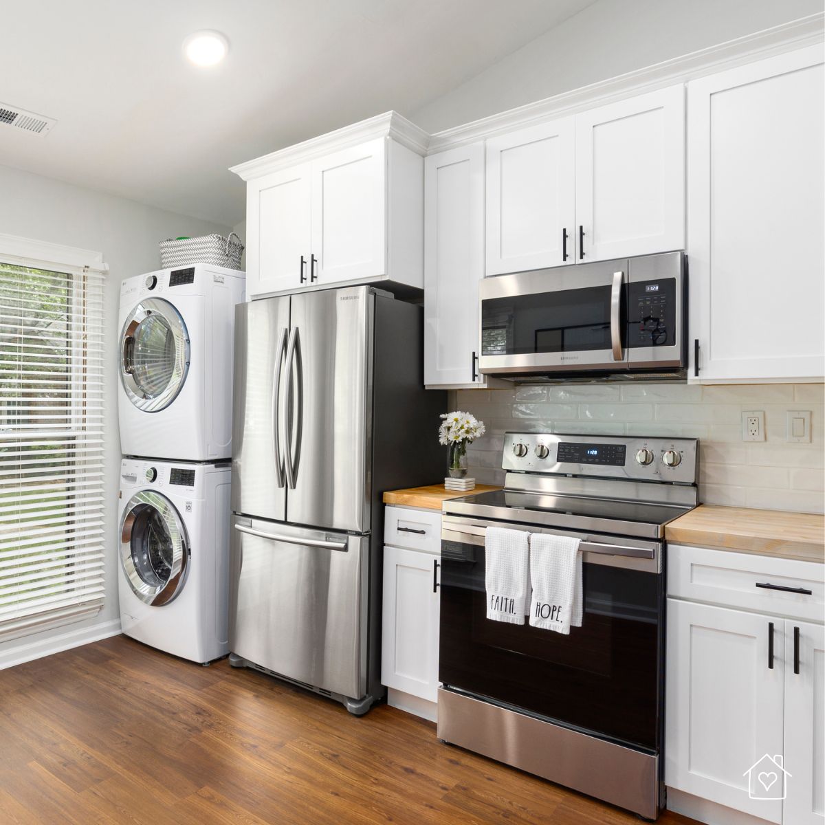 Sleek white kitchen featuring a stacked washer-dryer, stainless steel fridge, and modern stove, representing sustainable living with long-lasting appliances.