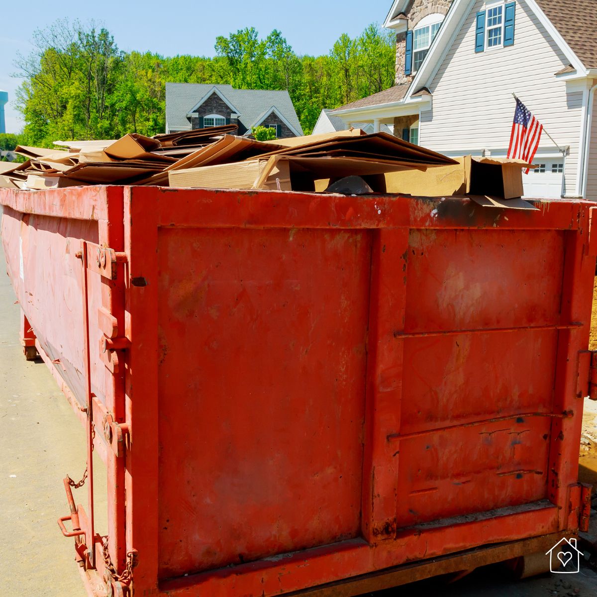 A large red dumpster placed in a residential neighborhood filled with renovation debris and discarded materials.