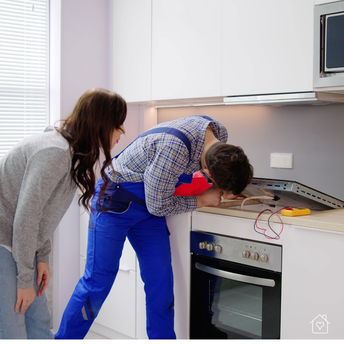 Service technician examining a built-in kitchen oven while a homeowner watches, highlighting professional appliance repair.