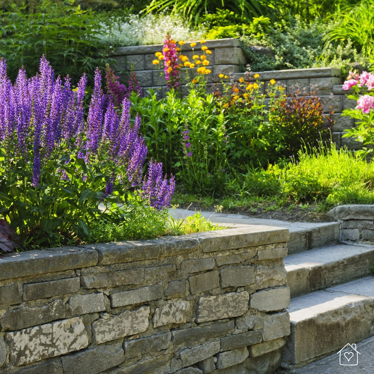 Beautiful raised garden bed made of stacked stone, filled with blooming flowers and lush greenery