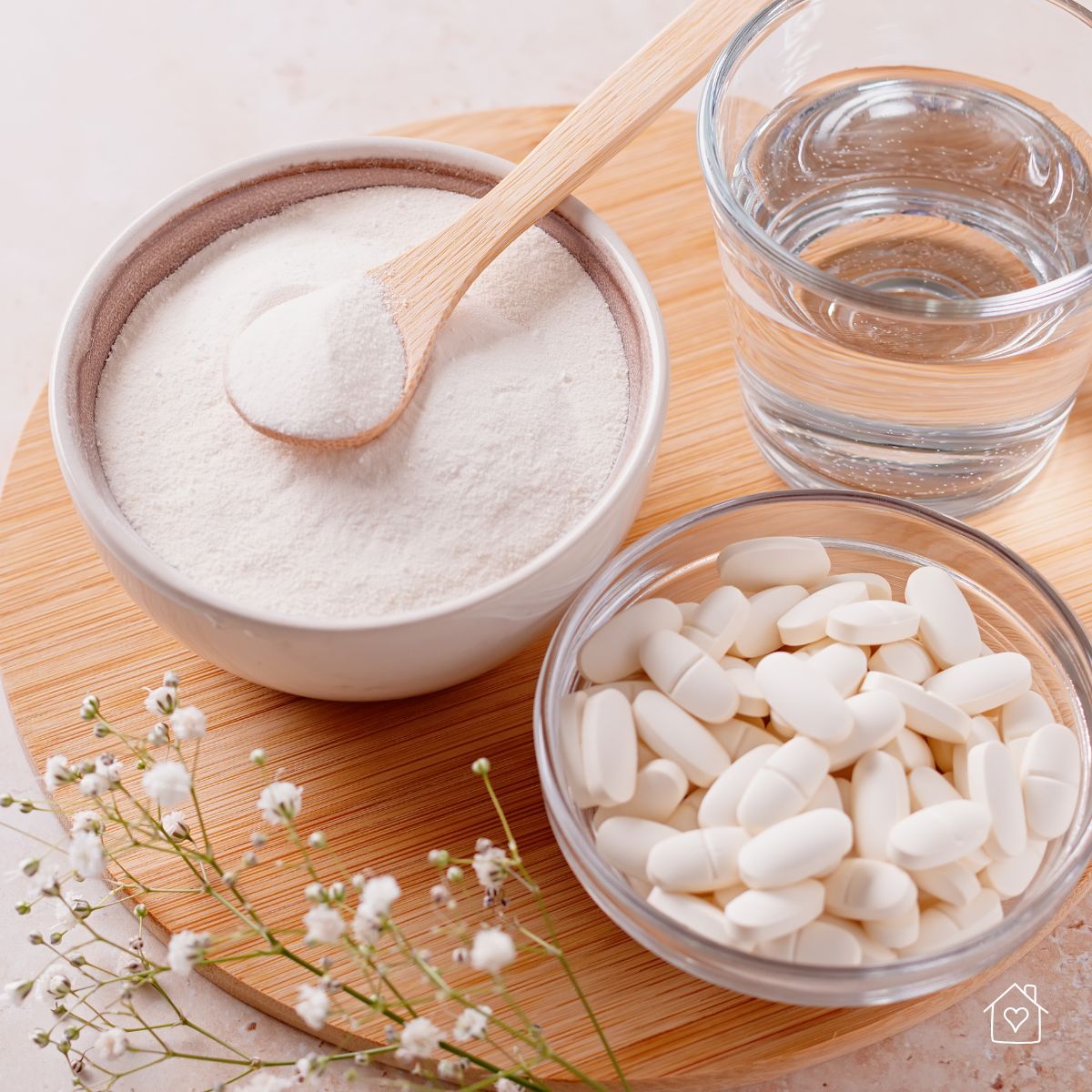 Bowl of collagen powder, glass of water, and bowl of collagen capsules displayed on a wooden tray for skin aging support.